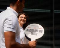 Two Sportsworld employees hold a sign saying 'Official England Travel' while welcoming fans at UEFA Euro 2024