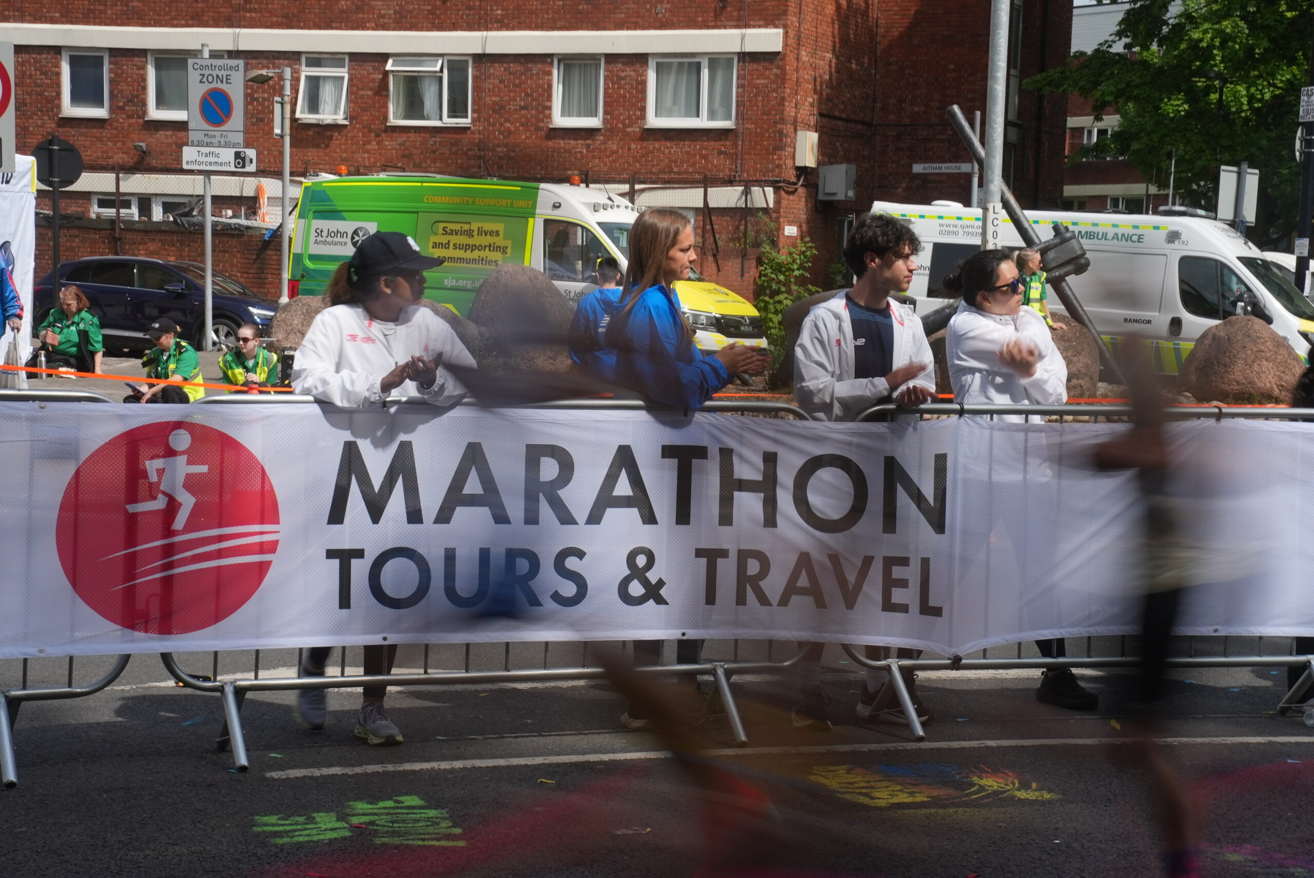 Supporters watch on at the London Marathon in front of a Marathon Tours & Travel branded logo